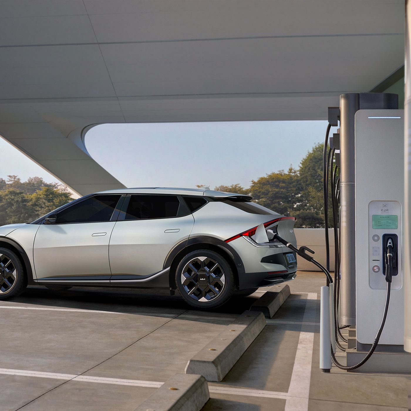 A sleek silver-white Kia SUV parked in a modern charging station lot, with an 800v DC fast charger connected to the driver's side rear charging port.
