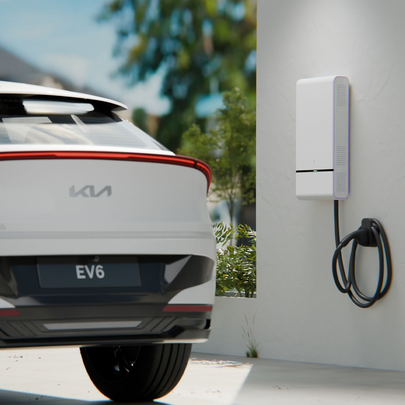 Outdoor shot of the rear of a white Kia EV6 parked next to a vehicle to home battery charging station mounted on an exterior wall, with cable coiled around a hook. Trees and a blue sky are visible in the background.