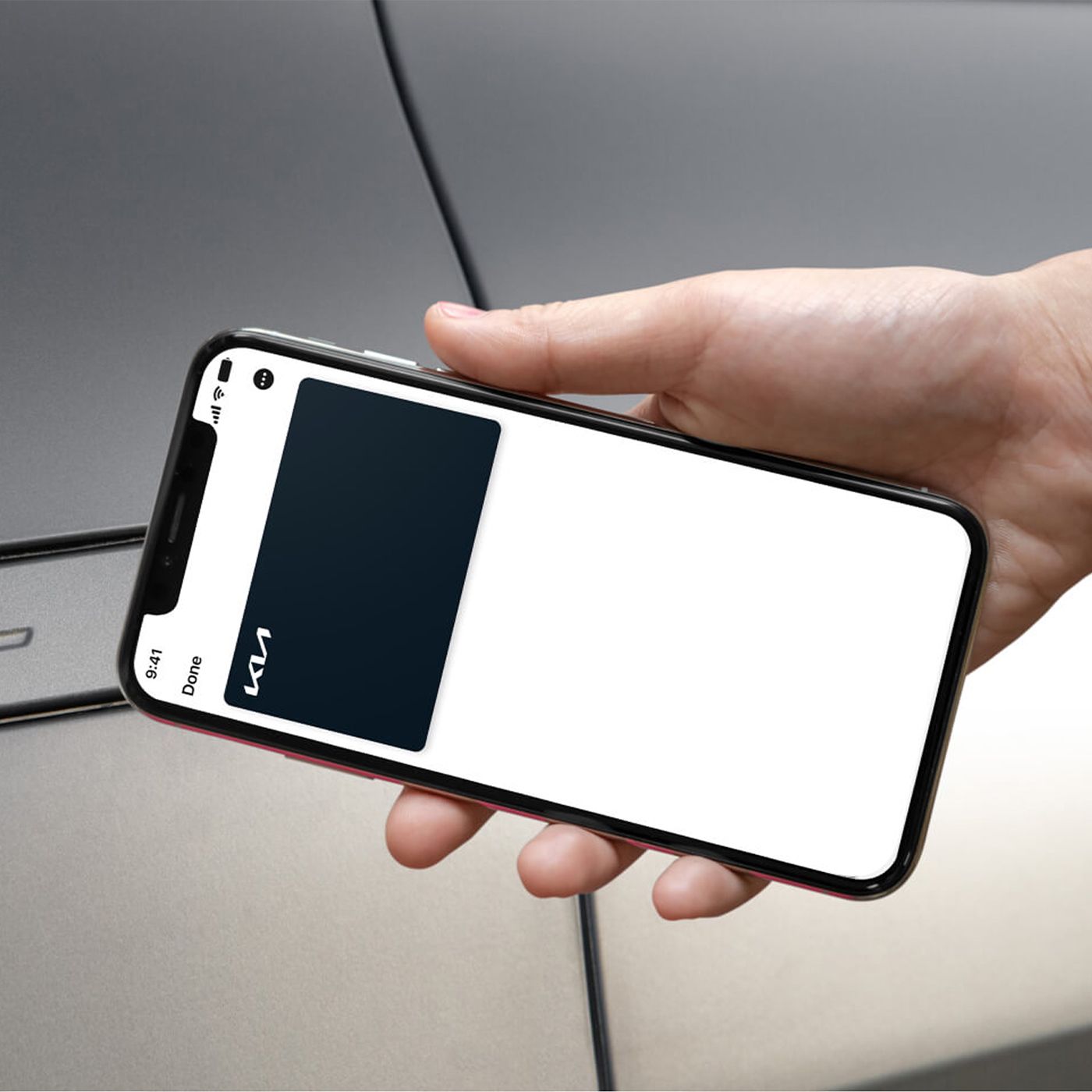 A hand holding a smartphone displaying Kia digital keycard app near a silver Kia vehicle door, showcasing keyless entry technology.