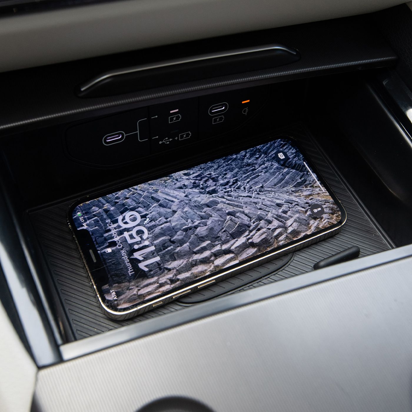 Close-up of the Kia interior wireless charging station with a smartphone halfway charged with a rocky landscape as the lock screen, highlighting advanced convenience and tech features.