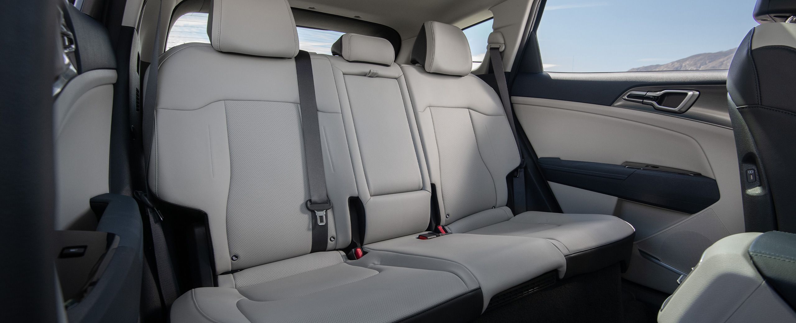 Interior view of the 2027 Kia Sportage Hybrid 2nd-row seating area in white featuring three headrests and showcasing the class-leading rear seat legroom, with blue cloudy skies visible through the window.