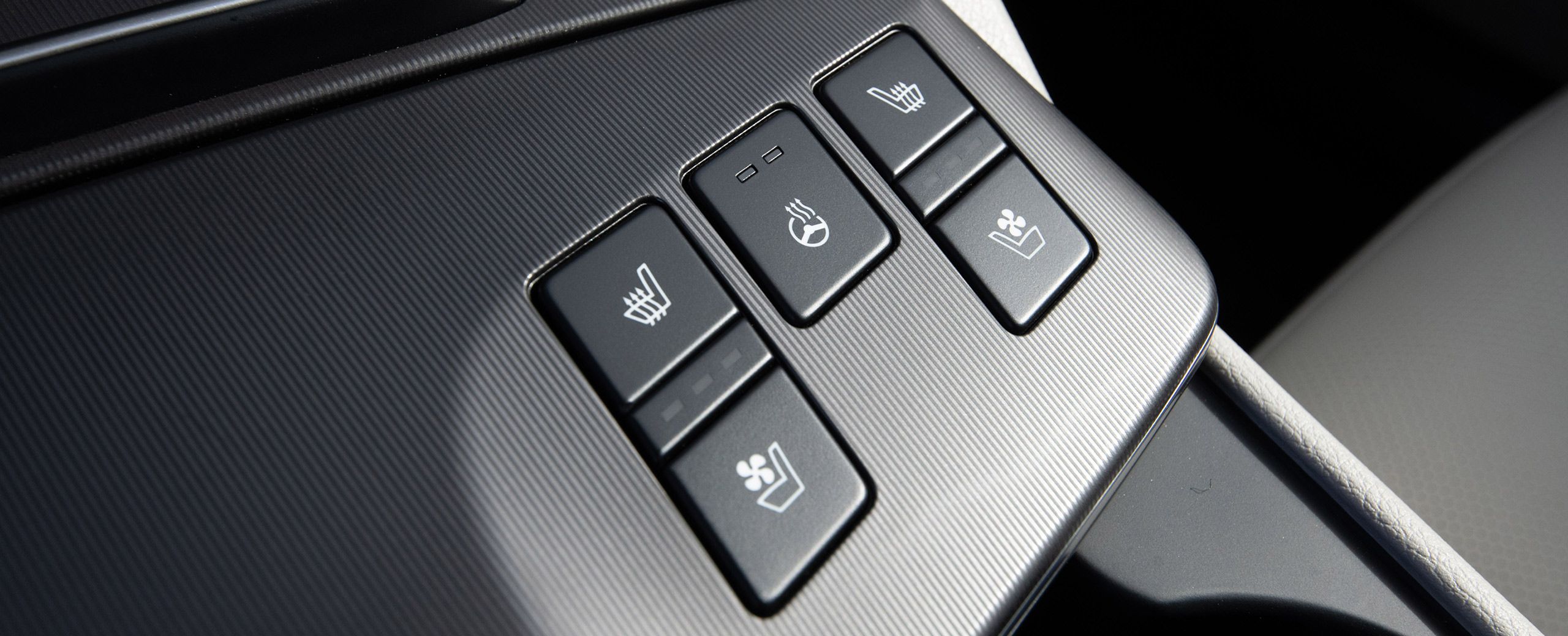 Zoomed-in photo of the black interior of the 2027 Kia Sportage Hybrid featuring 5 buttons that allow you to heat and ventilate seats and heat the steering wheel.