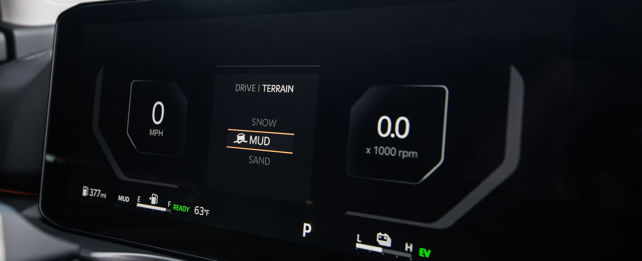 Close-up of the 2027 Kia Sportage Hybrid interior dashboard displaying miles per hour on the left, terrain mode in the middle with mud selected, and RPM on the right, highlighting the available all-wheel drive.