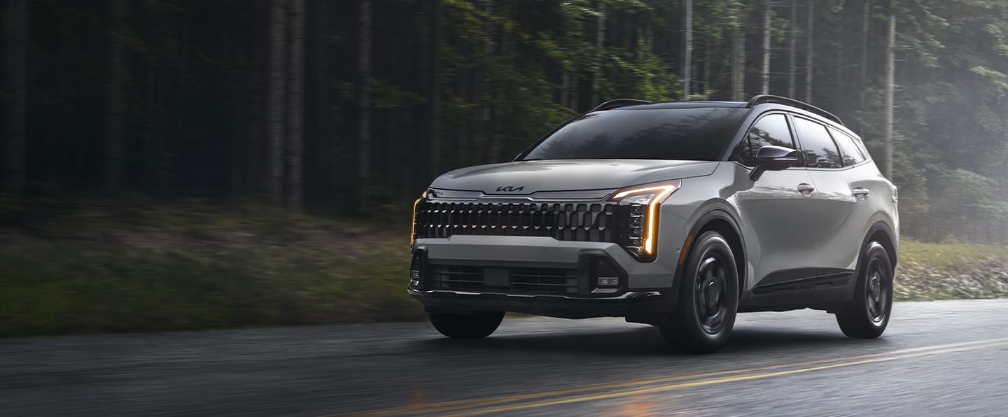 Silver 2027 Kia Sportage driving on a wet road through a forest