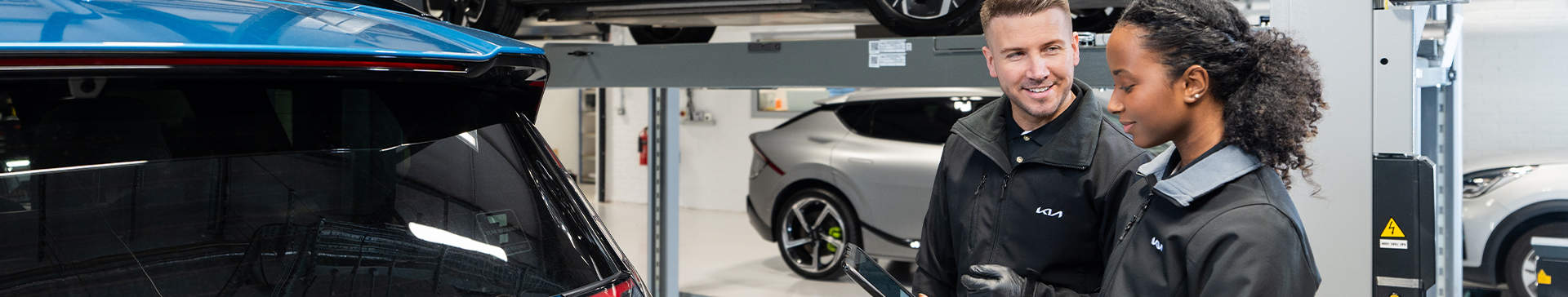 Two technicians standing next to a Kia EV9 in a garage.