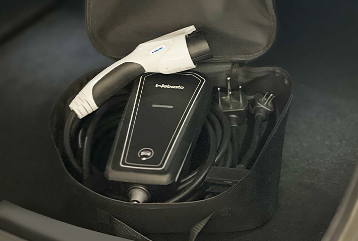 Primer plano del cargador portátil Webasto Go en su bolsa de almacenamiento en el baúl delantero de un vehículo eléctrico, primer plano