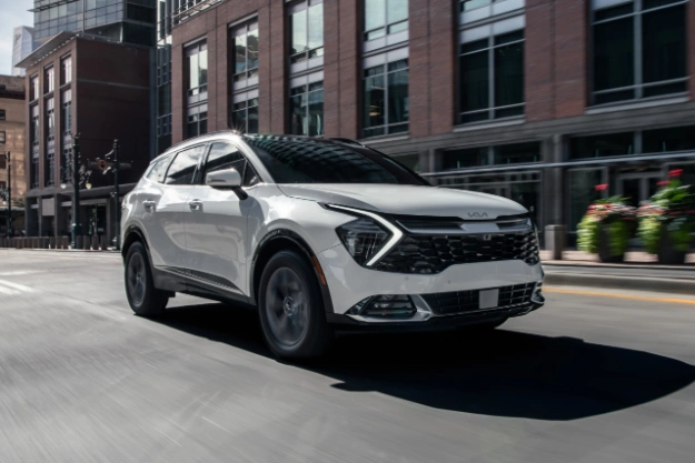 2024 Kia Sportage Hybrid in white driving down the city street in a three-quarter front view