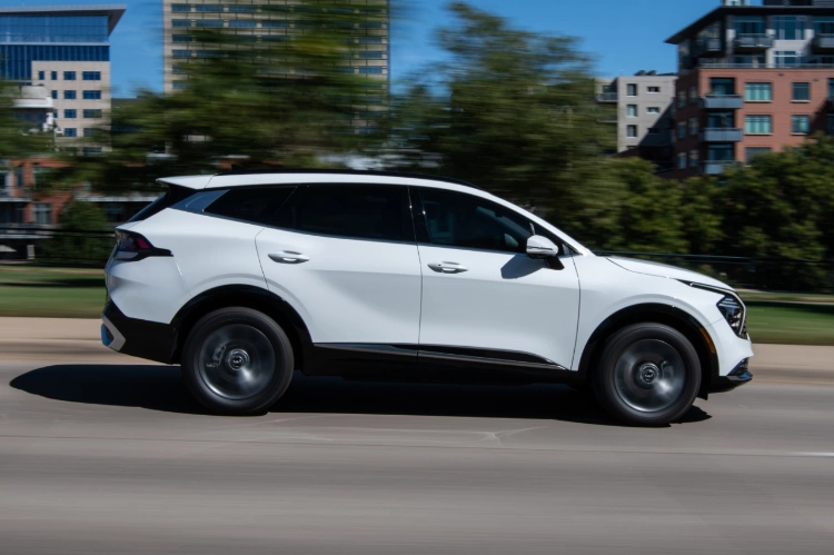 2024 Kia Sportage Hybrid in white driving by a park in a side view