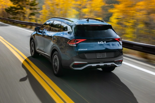 2024 Kia Sportage Hybrid in blue, three-quarter back view, driving through the mountains in the fall
