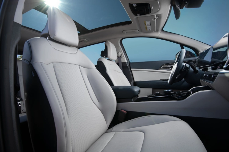 2024 Kia Sportage Hybrid interior, driver and passenger three-quarter view, featuring light grey leather seats and interior trim