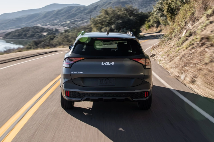 2024 Kia Sportage Plug-in Hybrid in matte gray, back view, driving down a mountain road