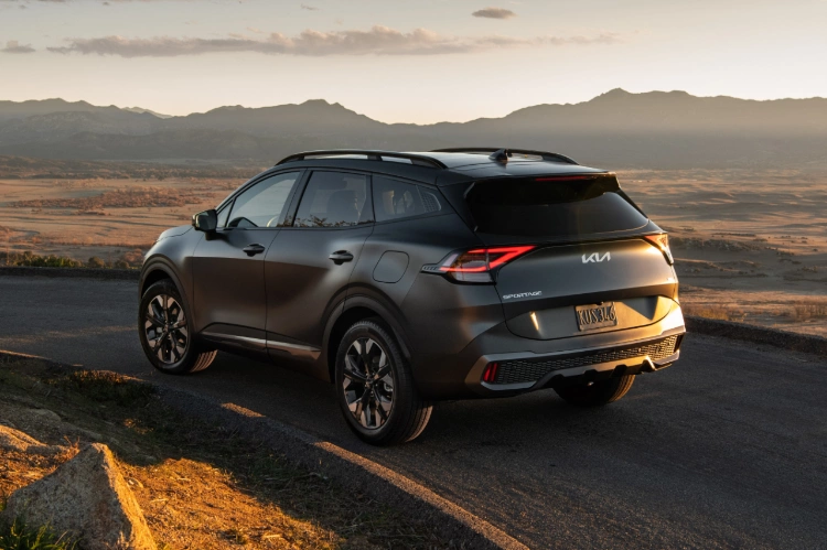 2024 Kia Sportage Plug-in Hybrid in matte gray, three-quarter back view, driving on a curved road in the mountains