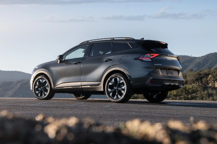 2024 Kia Sportage Plug-in Hybrid, in matte gray in a three-quarter back view, parked on a road in the mountains
