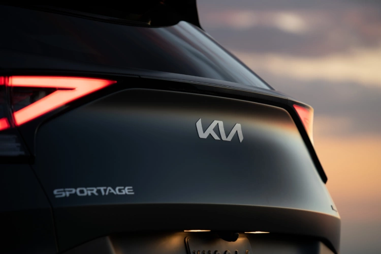 2024 Kia Sportage Plug-in Hybrid in matte gray, zoomed in three-quarter view of the back, with the tail lights glowing red and featuring the Kia emblem