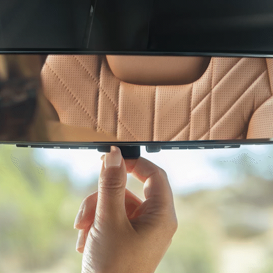 Interior del vehículo Kia, vista ampliada del espejo retrovisor con pantalla digital que muestra árboles y arbustos en la pantalla