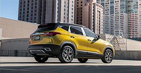 Rear passenger-side three-quarter view of a yellow Kia SUV parked in an urban landscape.
