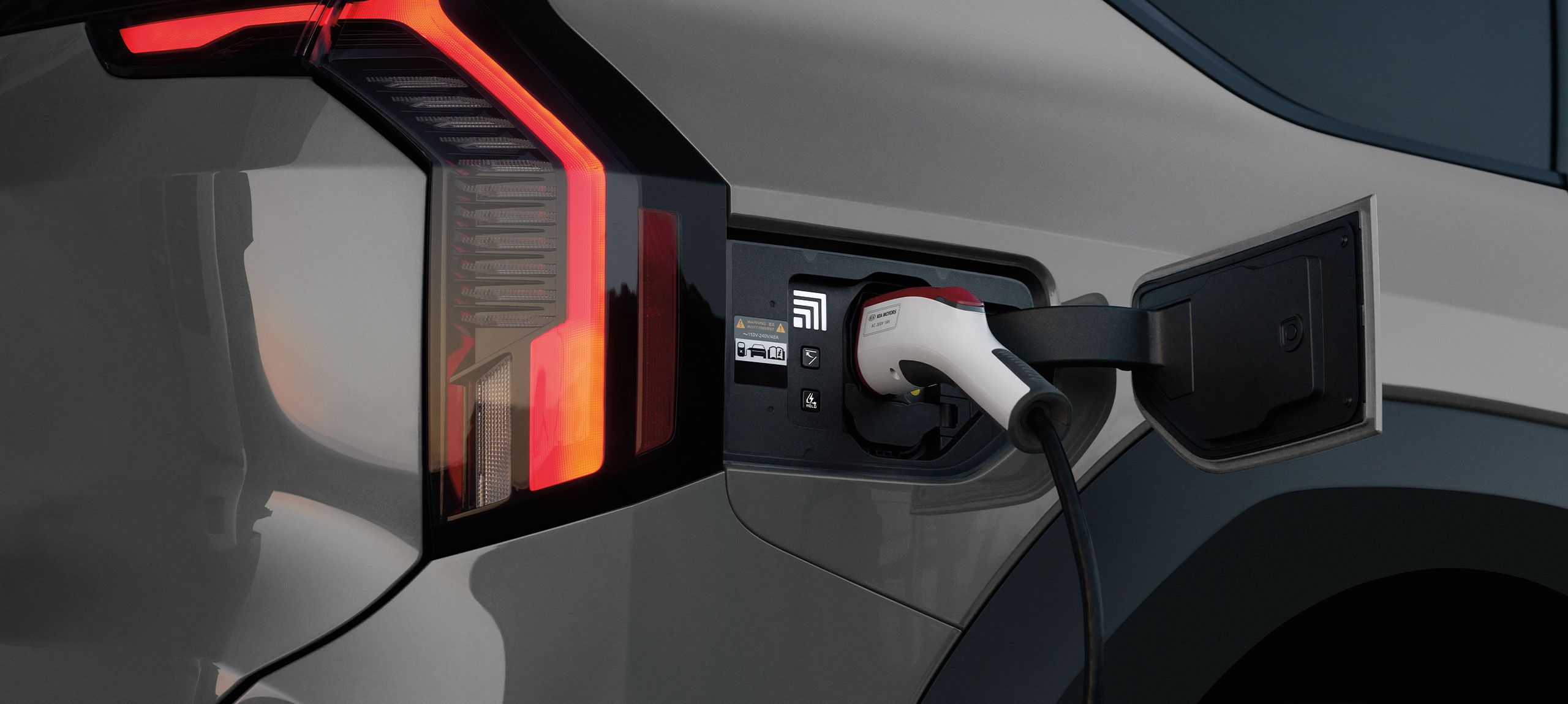 Close-up of a charging cable plugged into the charge port of a Kia EV9, shown for illustration
