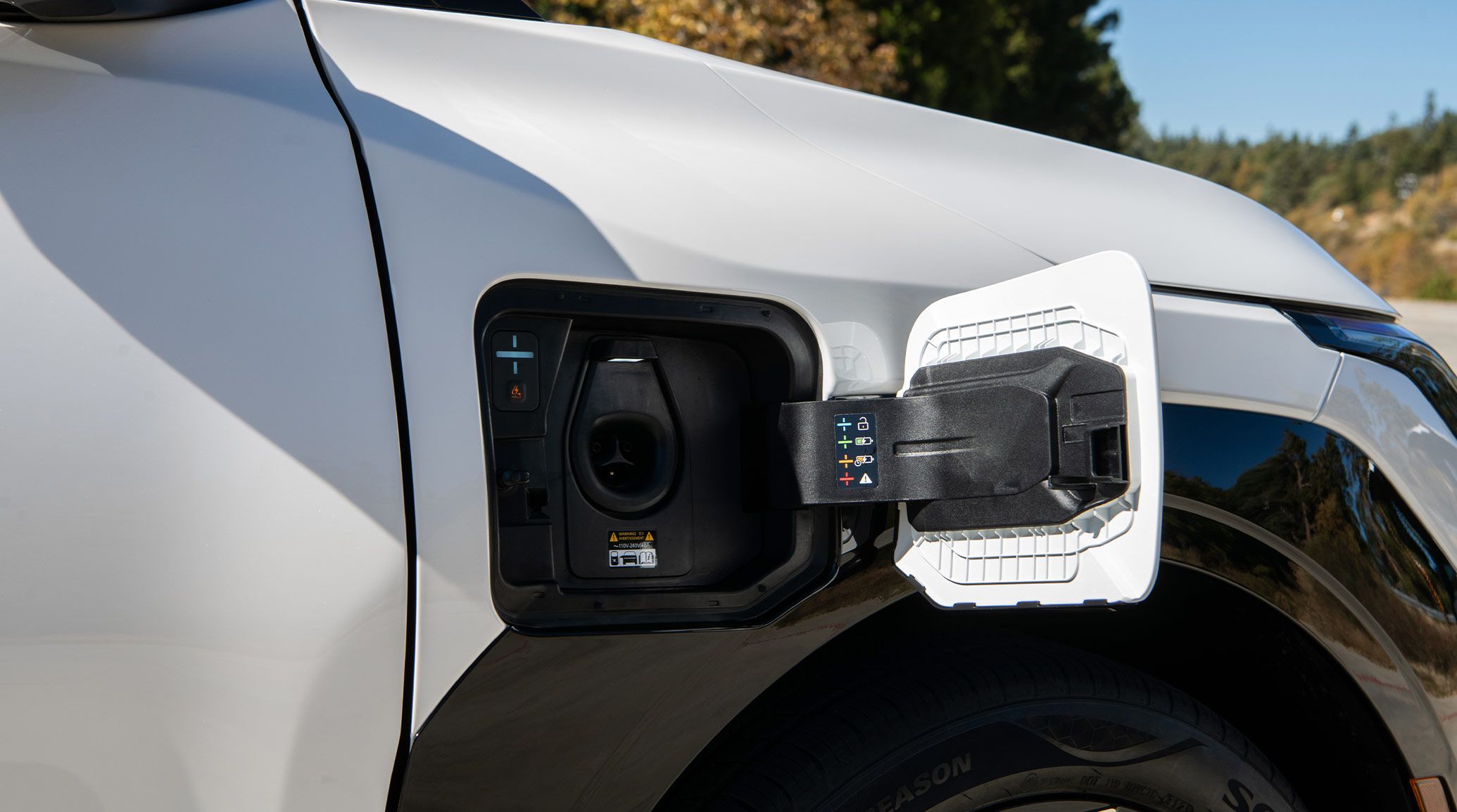 Close-up photograph of the opened electric battery charging port door on the 2027 Kia EV3 compact electric SUV, with socket and decals explaining light color meanings.