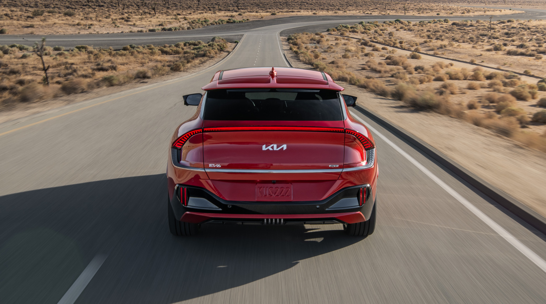 A photo of the back of a red 2023 Kia EV6 speeding down the road in the desert