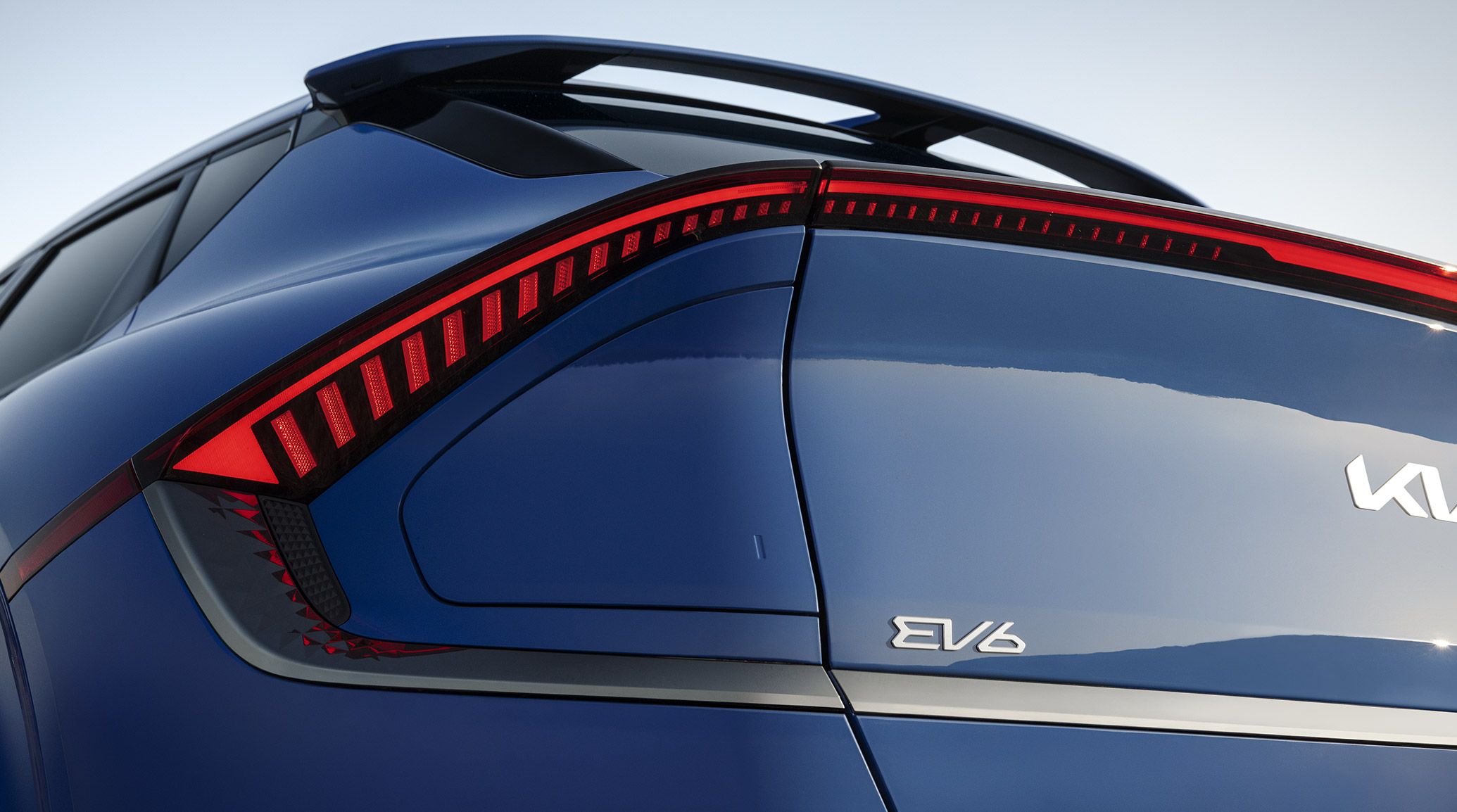 Low close-up angle of the driver's side closed charging port and red LED taillights on the 2026 Kia EV6 electric CUV GT-Line AWD in blue. The KIA and EV6 stylized emblems are visible on the back of the vehicle.