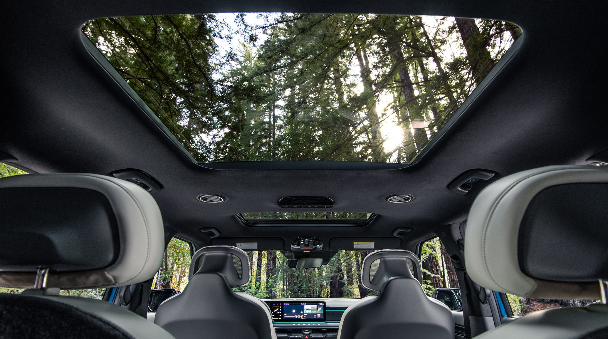 2024 Kia EV9 interior, three-quarter roof view from the back of the vehicle, highlighting the panoramic sunroof that gives an expansive view of the forest trees