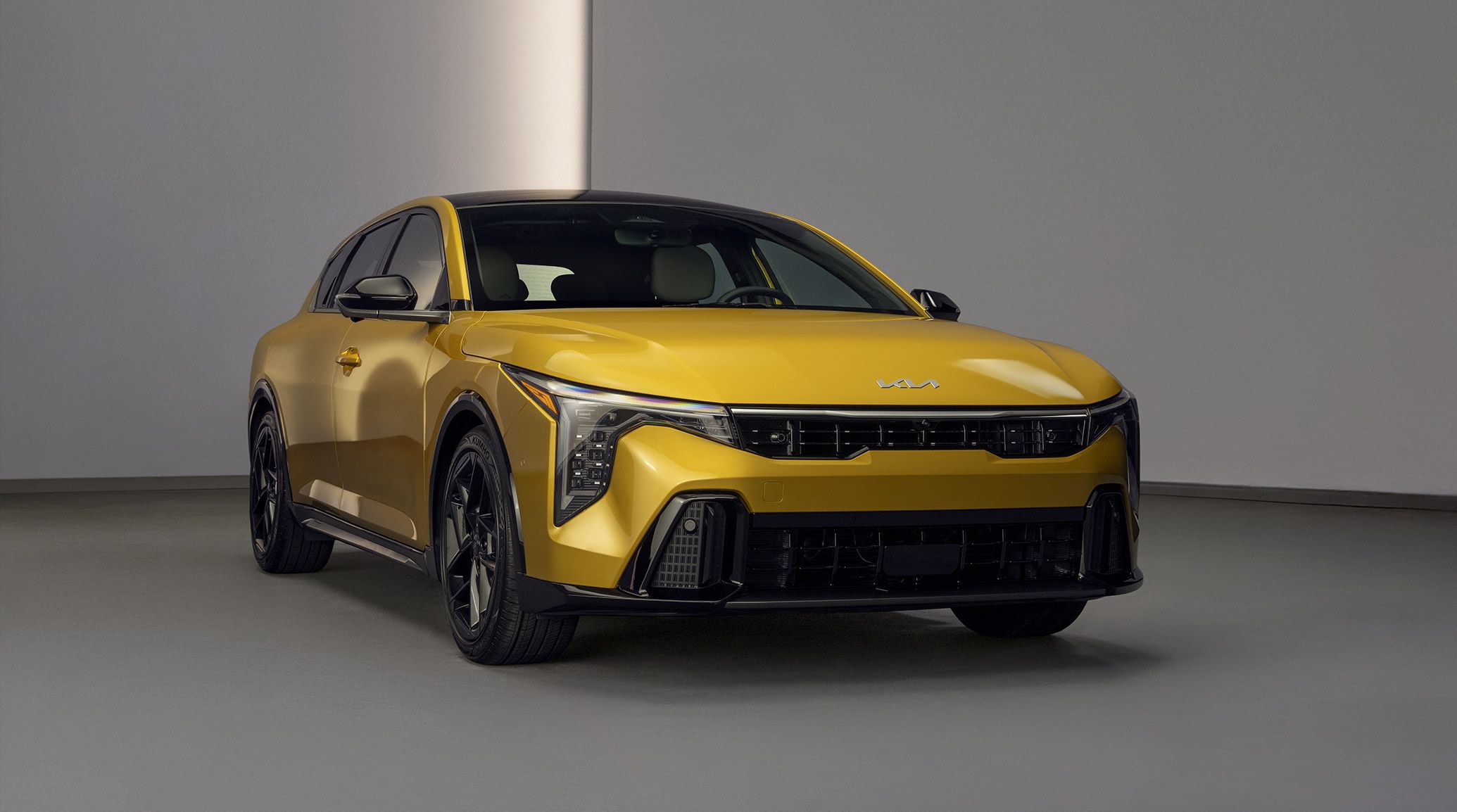 Front three-quarter exterior view of the 2026 Kia K4 Hatchback GT-Line Turbo in sparkling yellow parked in a white room, featuring the LED cube projector headlights and sport-inspired details.