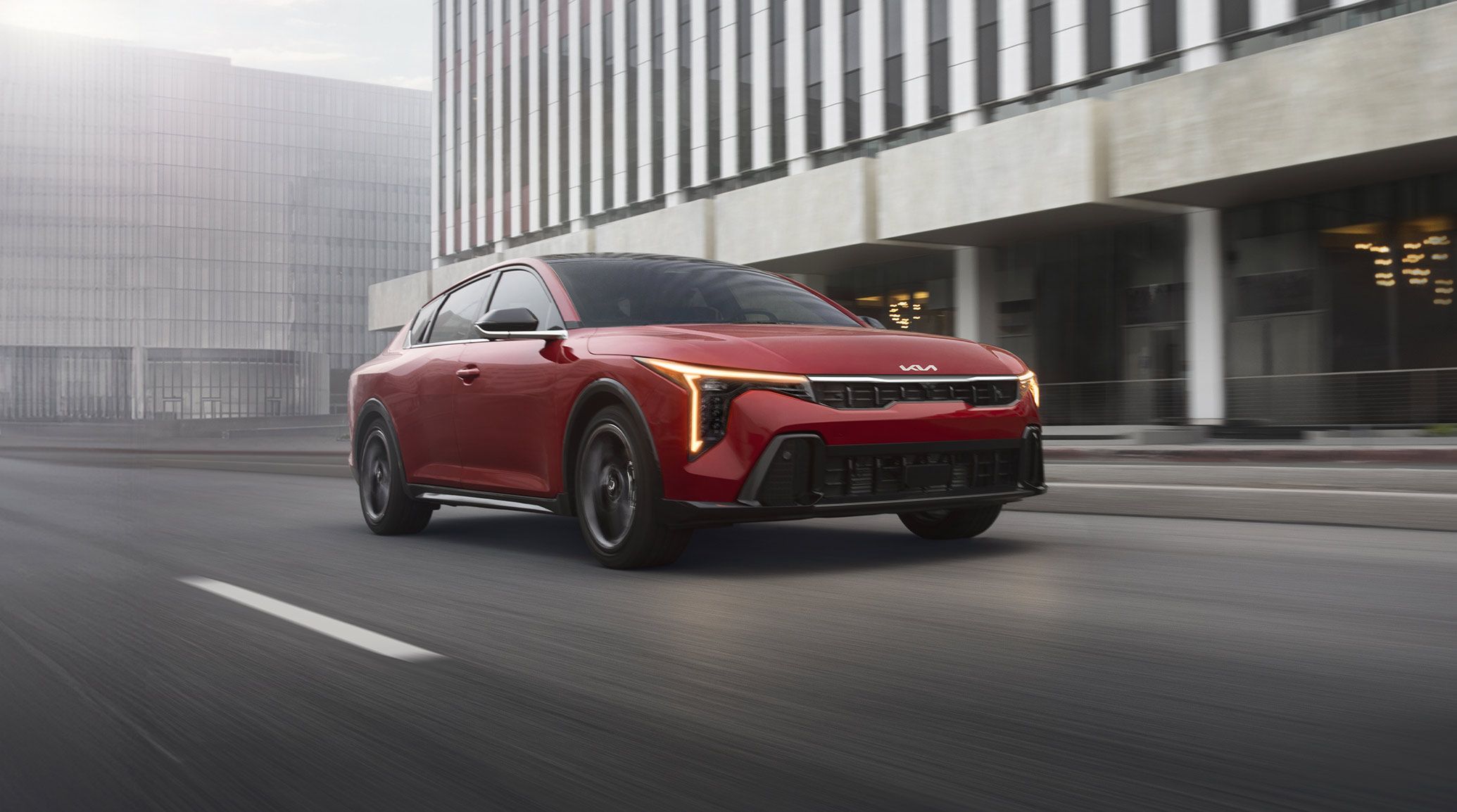 Dynamic shot of the 2027 Kia K4 in red, looking stylish as it drives through a foggy urban city environment, highlighting the sleek body design.
