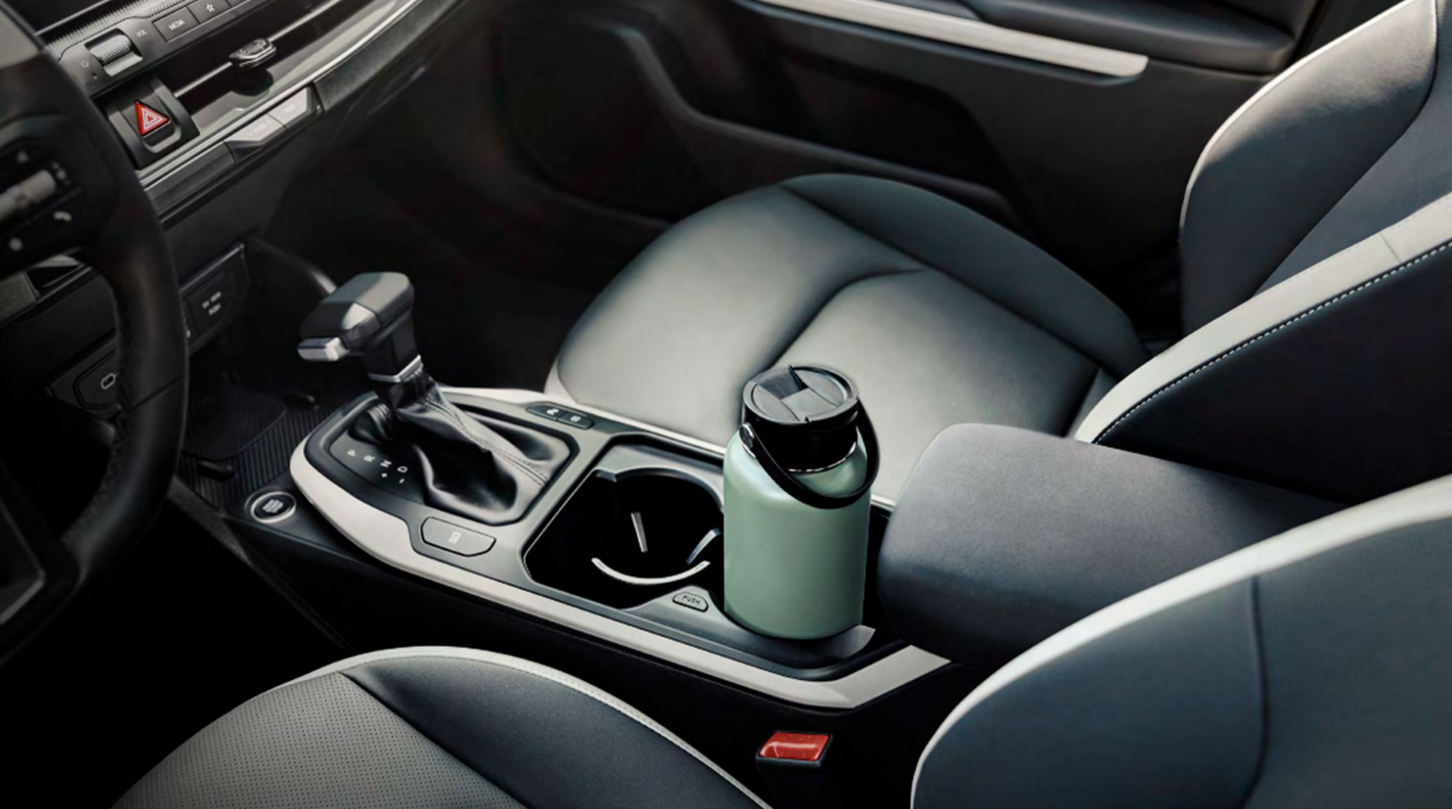 Interior view of the 2027 Kia K4 center console, including the shifter and large cup holders, one of which is currently holding a reusable light green water bottle.