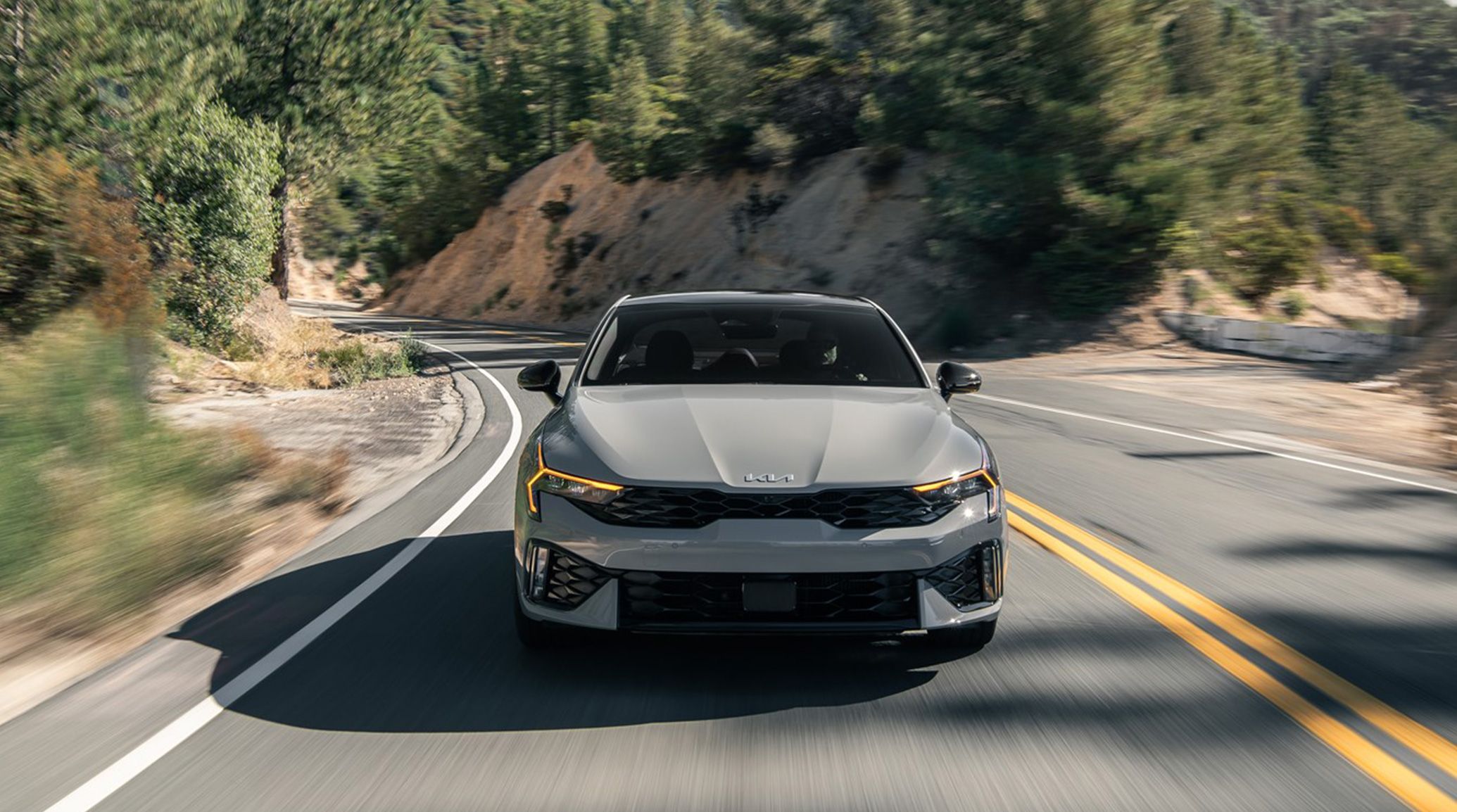front view of 2025 Kia K5 driving down a two way mountain road.