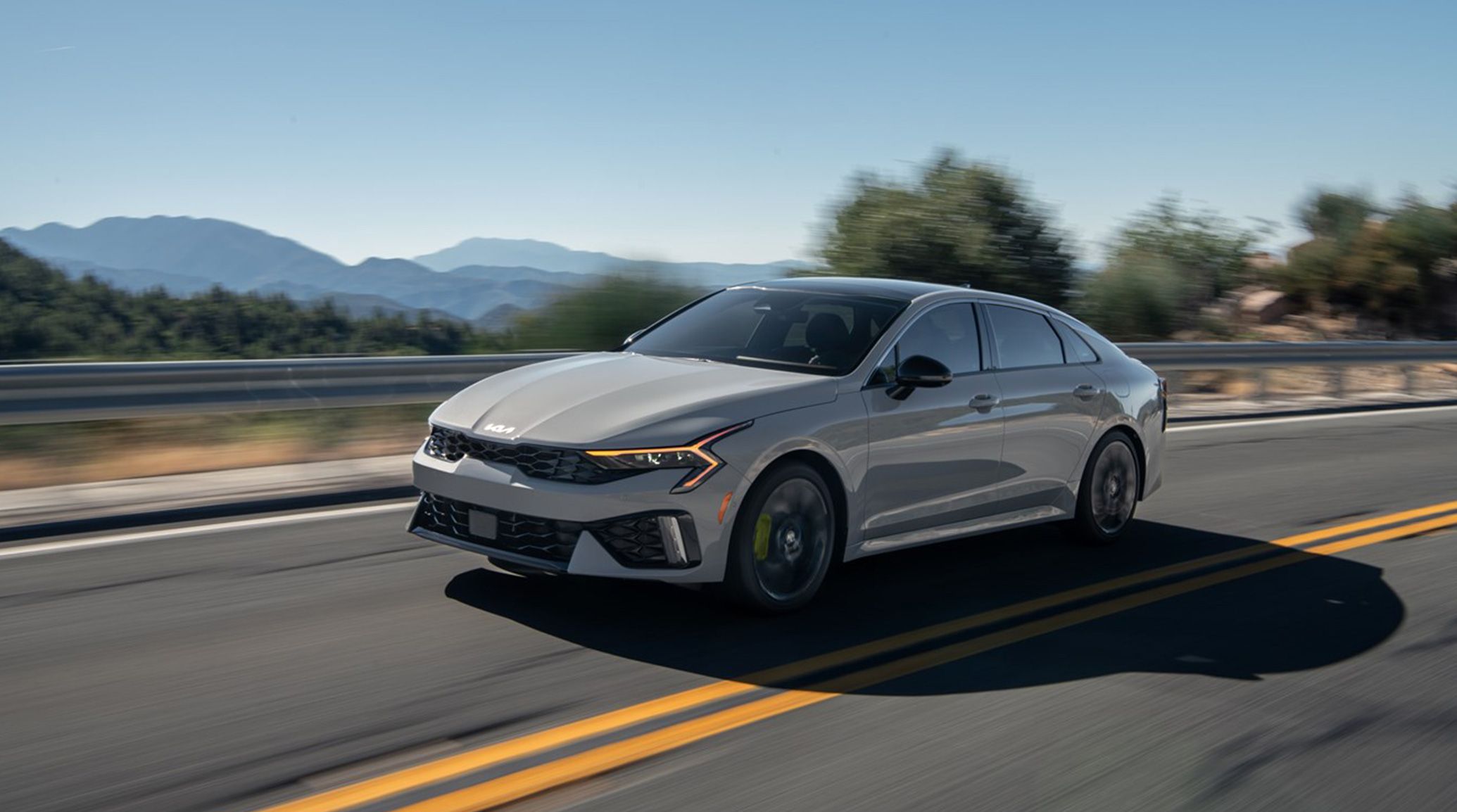 2025 Kia K5 with grey exterior driving down a two lane highway