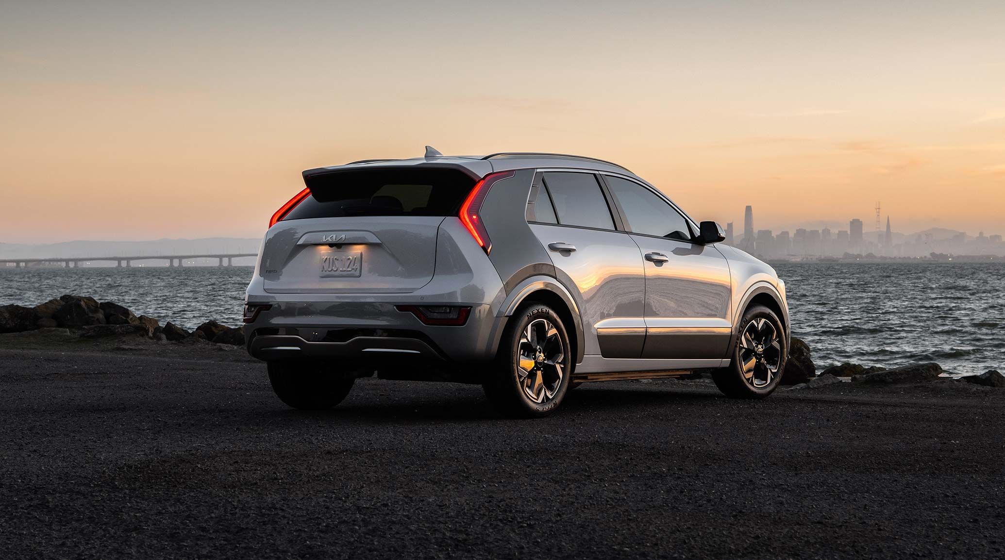 2026 Kia Niro EV, three-quarter back view, parked overlooking a bay at sunset, with the LED taillights on
