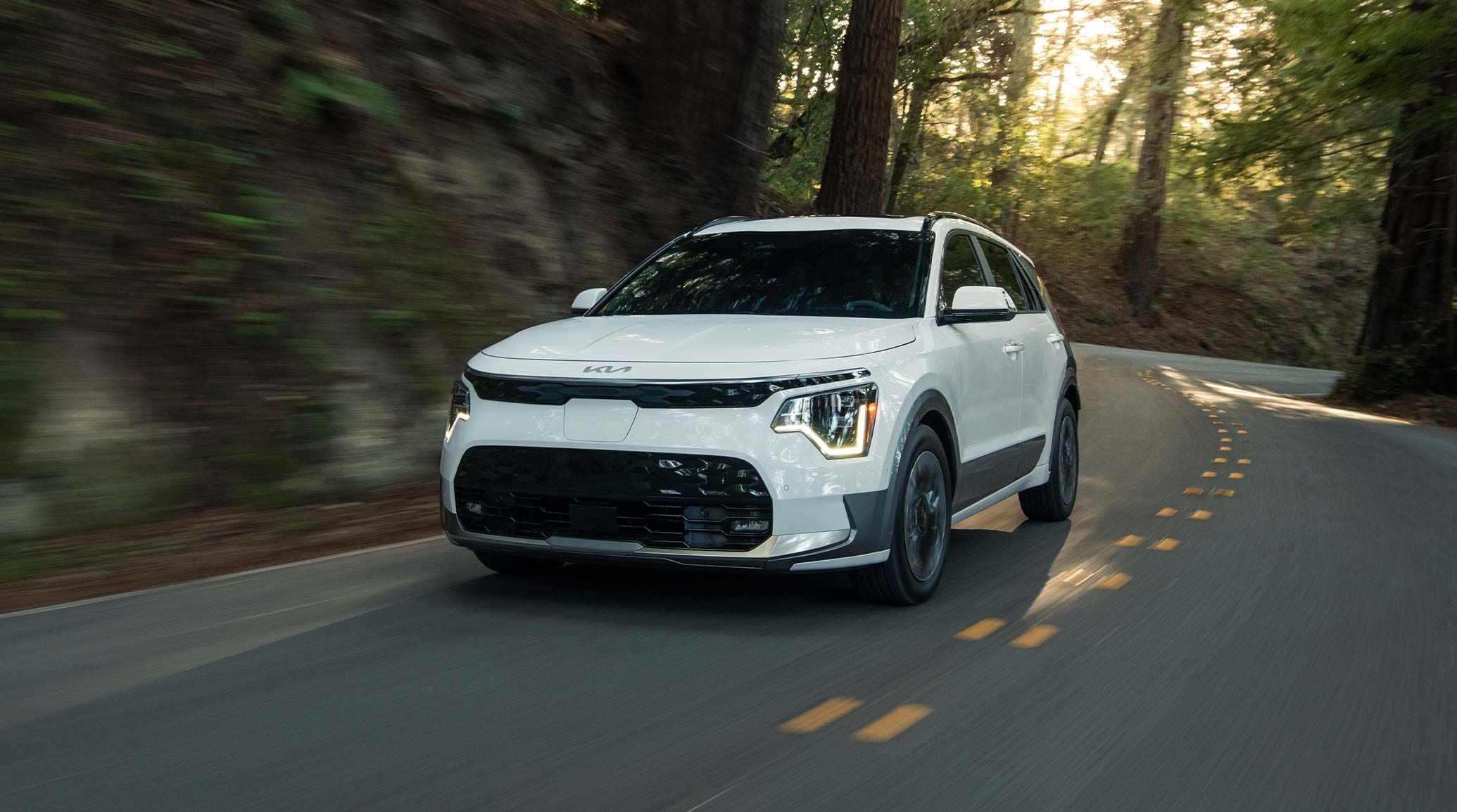 2026 Kia Niro EV driving through a forest road, front three-quarter view
