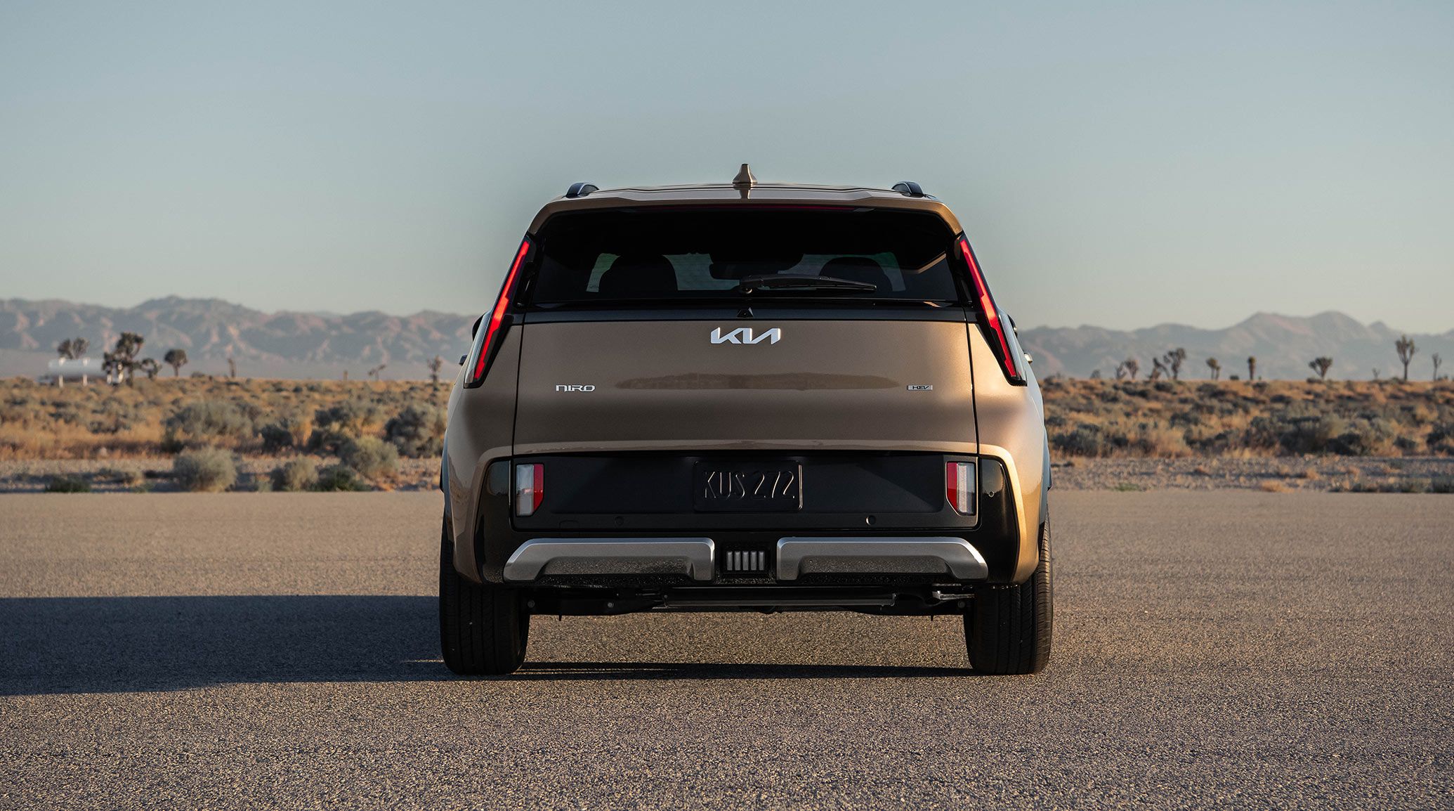 Rear photograph of the 2027 Kia Niro Hybrid subcompact SUV showing the silhouette from behind, including chrome rear bumper and black trim. A desert background is visible in the distance.