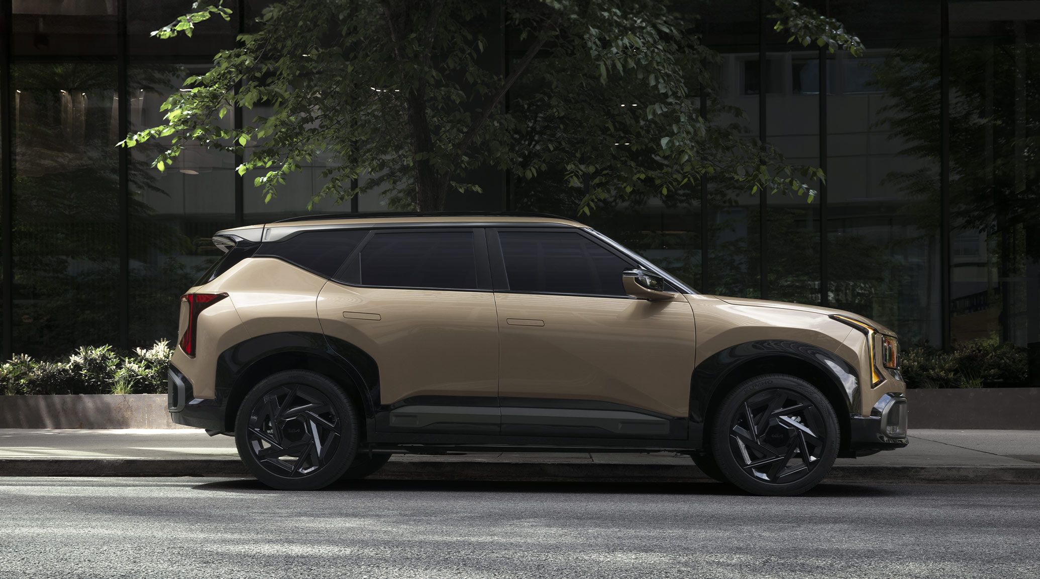 2027 Kia Seltos X-Line SX AWD in brown parked on a road with greenery and a building behind it, shown in full side profile with black wheels and rugged styling highlighted.