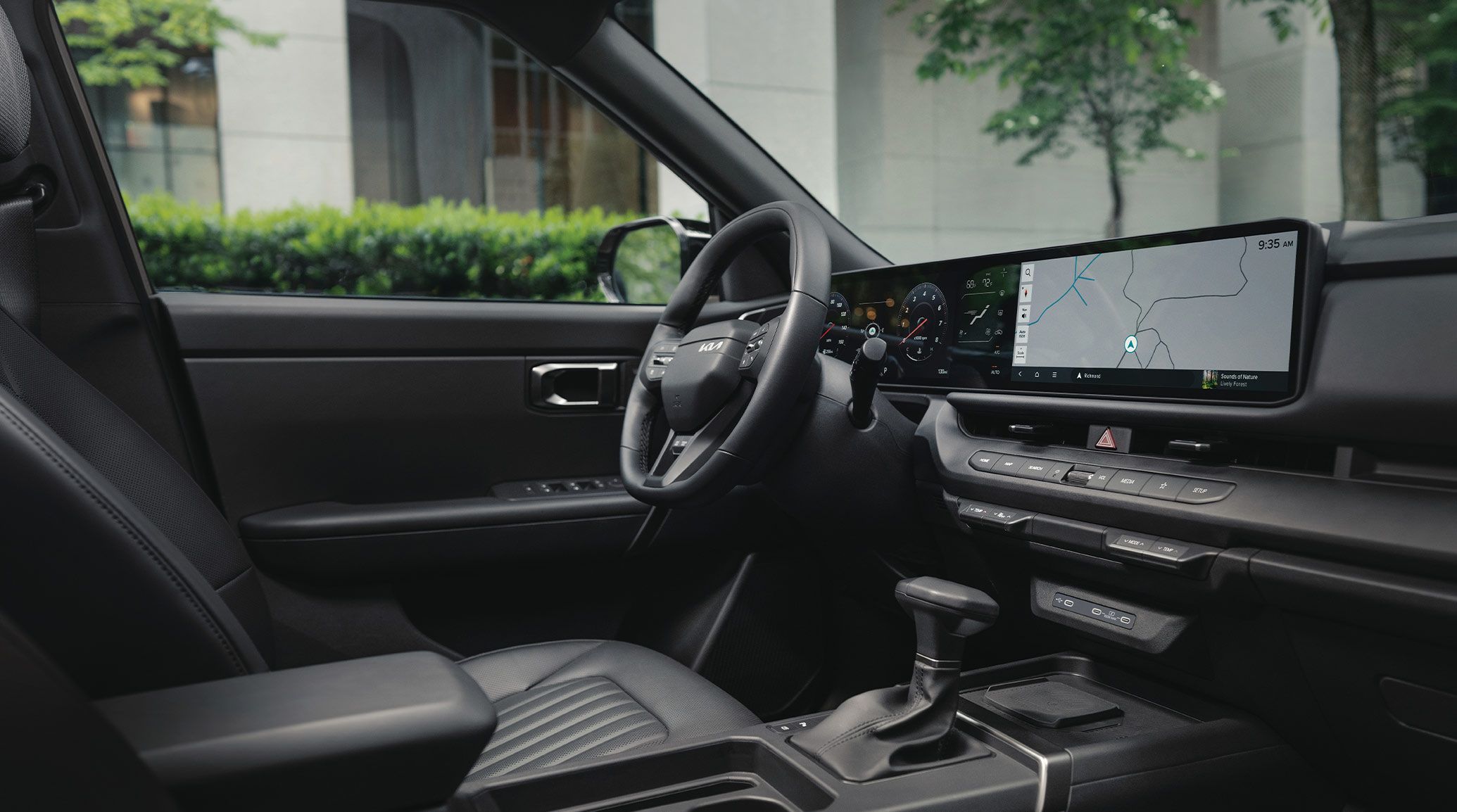 Interior of the 2027 Kia Seltos SUV featuring a modern black cabin with a modern steering wheel, leather seats, and a wide panoramic digital display with navigation displayed on the touchscreen. Trees and a house are visible through the windshield.