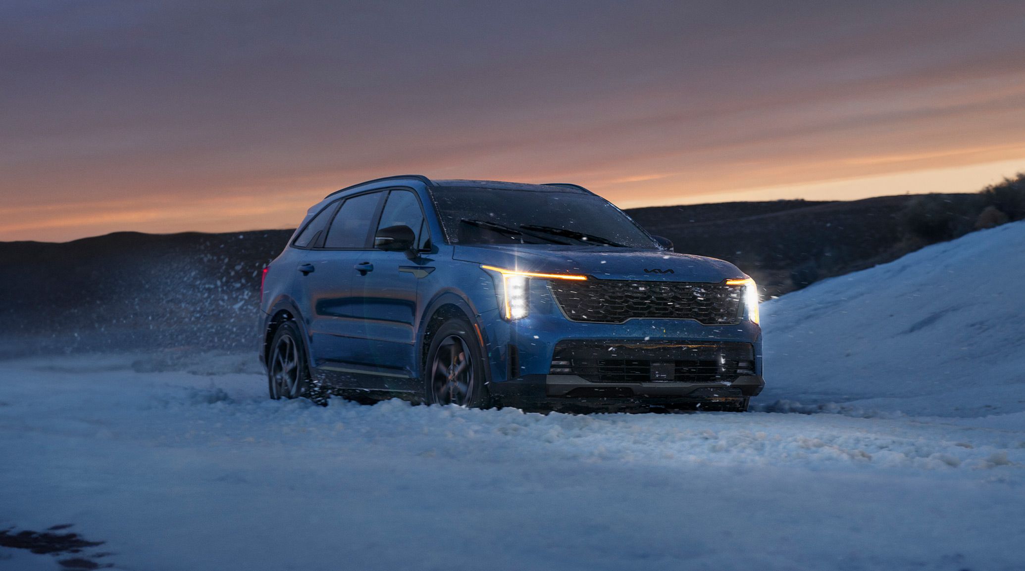 2026 Kia Sorento Hybrid, three-quarter front view, with the headlights on driving through snow