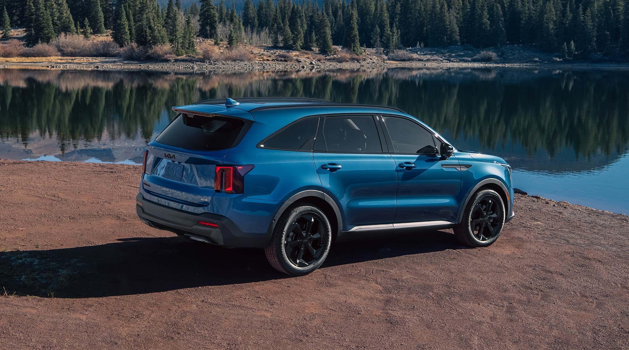 2026 Kia Sorento Hybrid in blue, three-quarter back view, parked in front of a lake in the forest