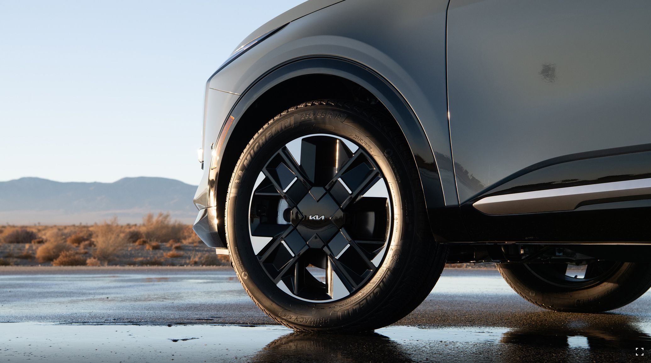 A close-up shot of the 2027 Kia Sportage Hybrid 19-in. distinctive front wheels parked on a wet road with mountains and plants in the background.