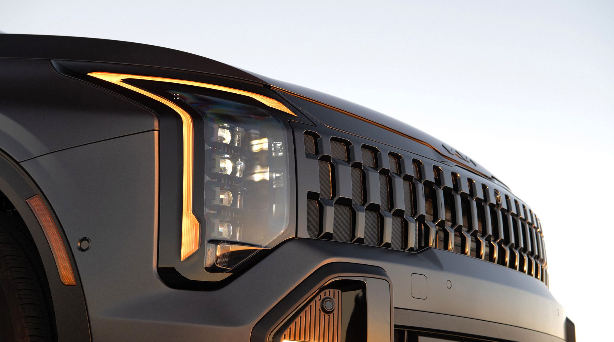 Close-up shot of the 2027 Kia Sportage Plug-In Hybrid in black featuring a bold gloss black front grille and LED headlights, set against a blue sky.