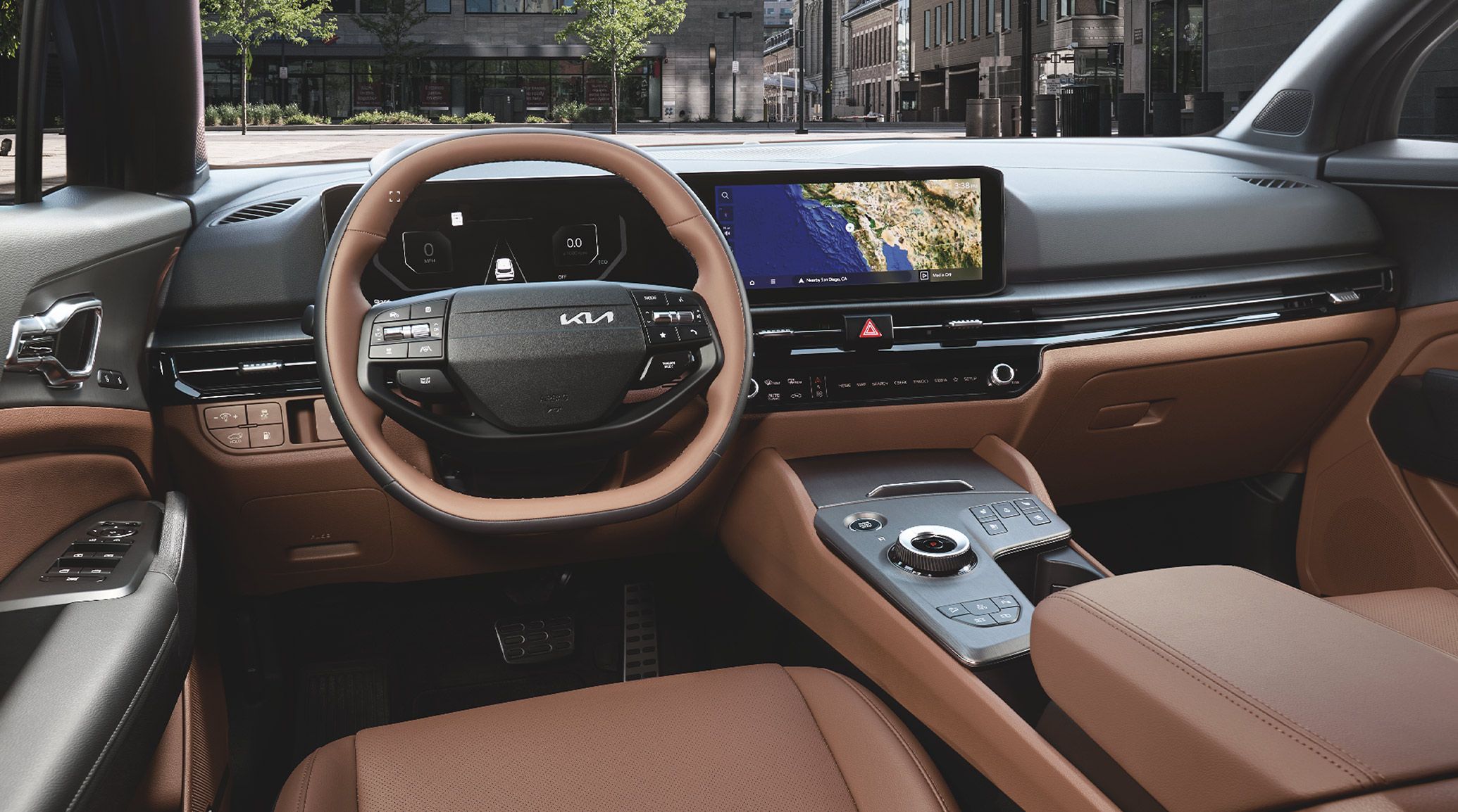 2027 Kia Sportage Plug‑In Hybrid interior from the driver’s perspective, featuring a wide digital display with navigation, the steering wheel, brown leather seating, and a modern center console with a rotary gear selector.