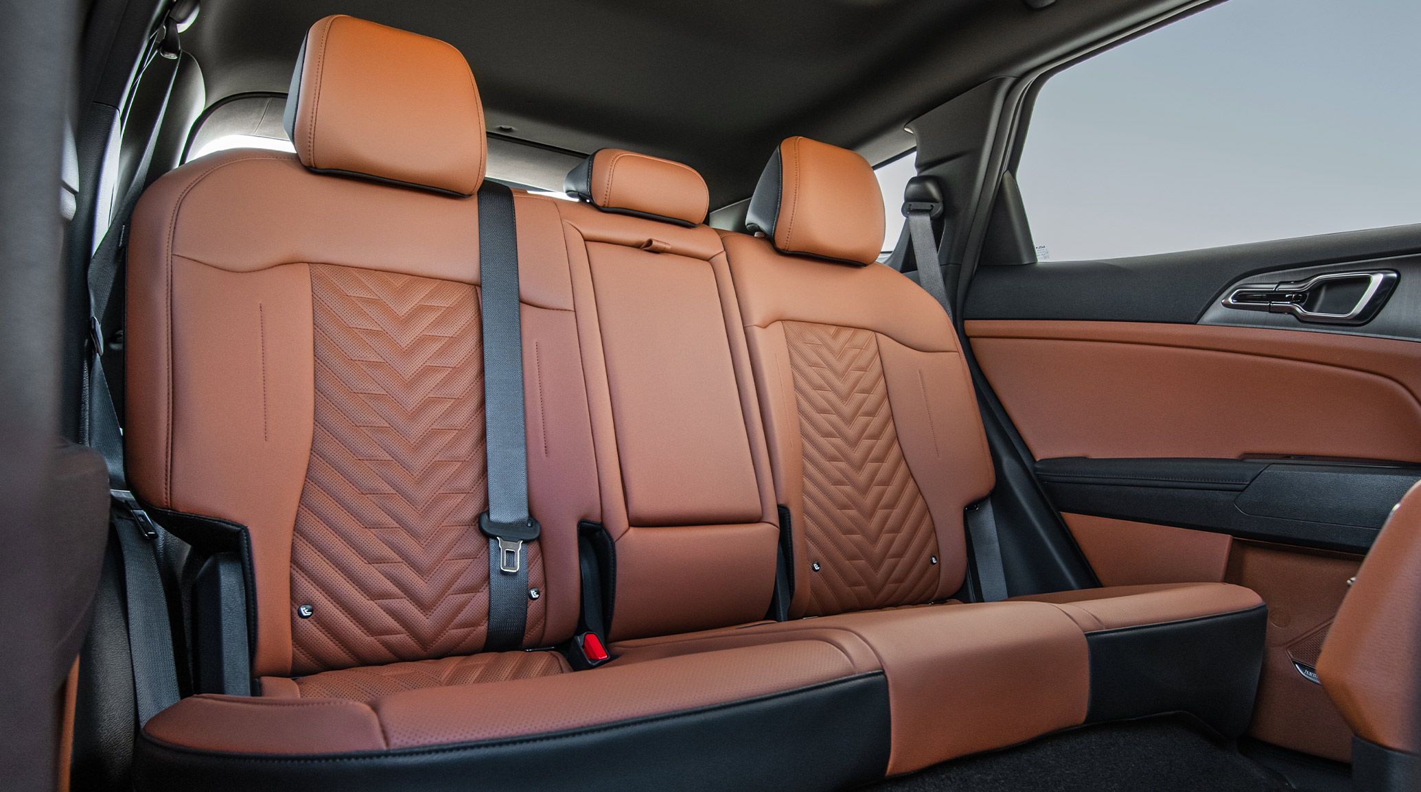 Interior view of the 2027 Kia Sportage Plug-In Hybrid 2nd-row seating area in brown featuring three headrests and showcasing the class-leading rear seat legroom, with blue skies visible through the window.