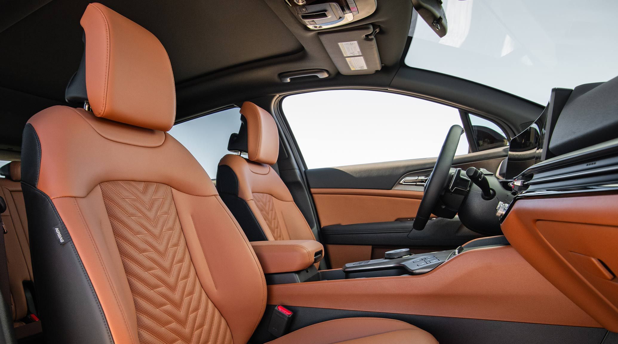 Interior view of the 2027 Kia Sportage SUV showcasing the perforated and quilted red-brown front seats. A blue sky is visible through the windows.