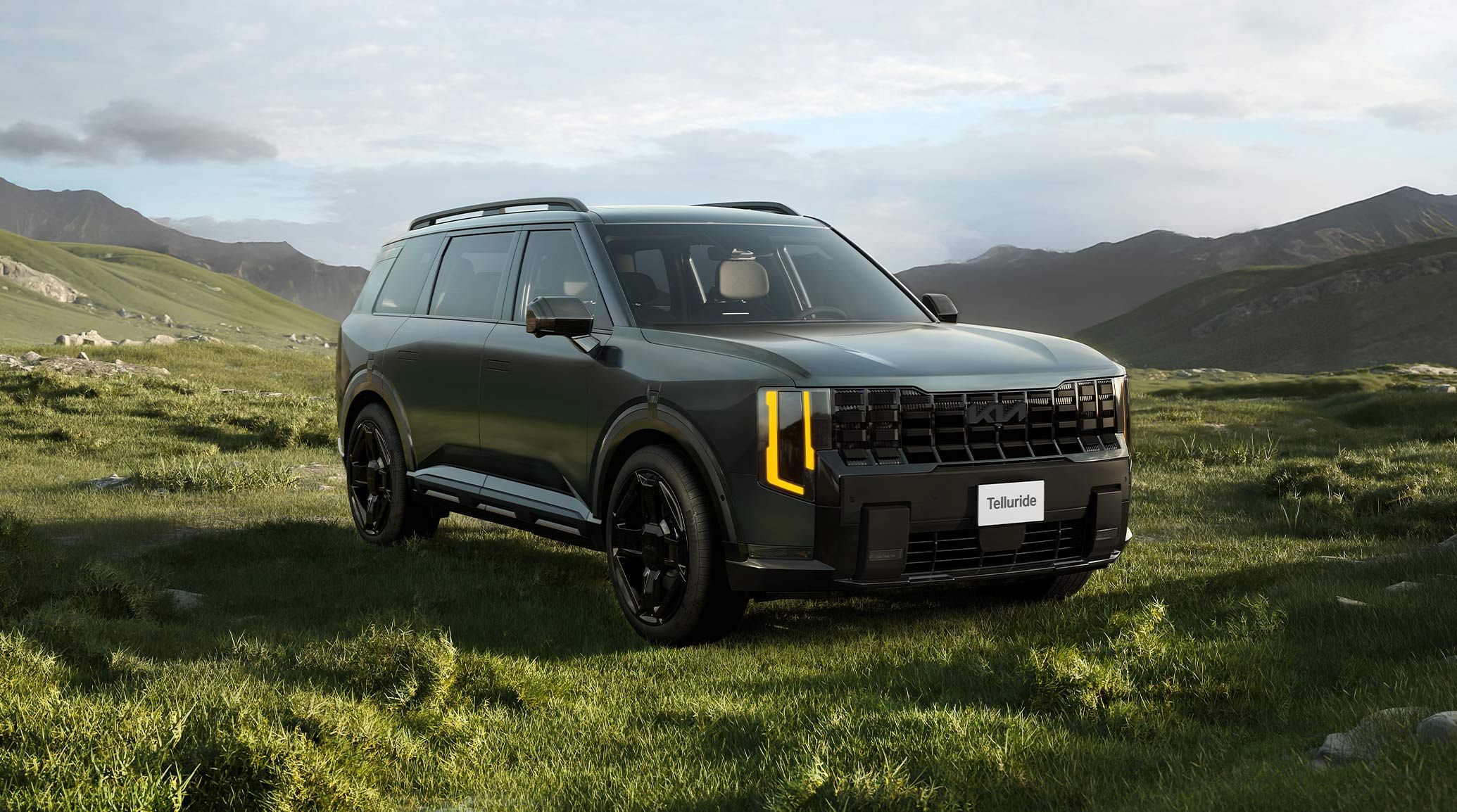 A front three-quarter view of the 2027 Kia Telluride HEV in jade green, featuring a bold front design, vertical headlights, and a front license plate saying Telluride. The SUV is parked on a grassy meadow with mountains behind it.