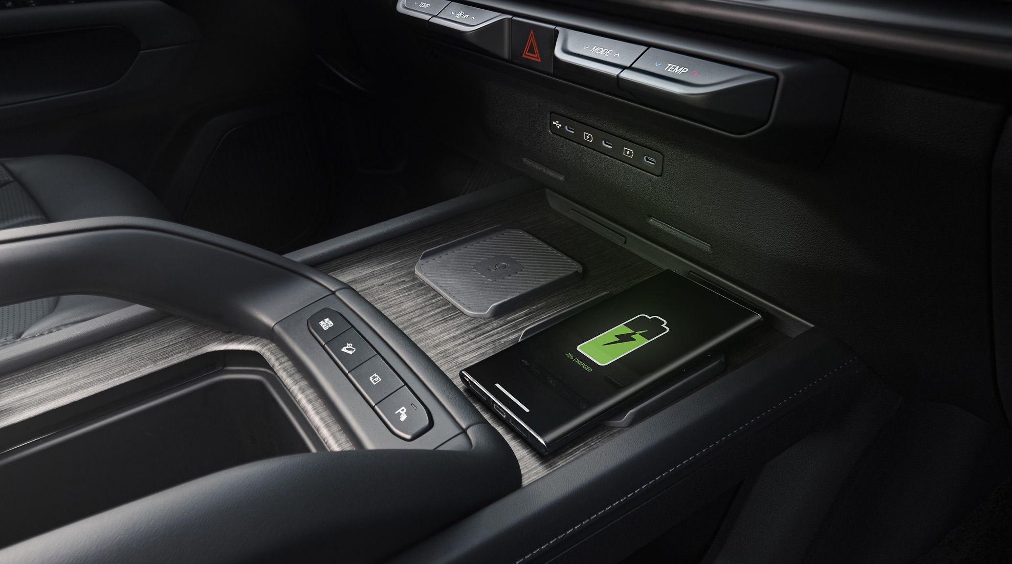 A up-close shot of the black interior of the 2027 Kia Telluride Hybrid center console area, featuring spacious cup holders and a wireless charging station with a smartphone on fully charged, highlighting advanced convenience and tech features.