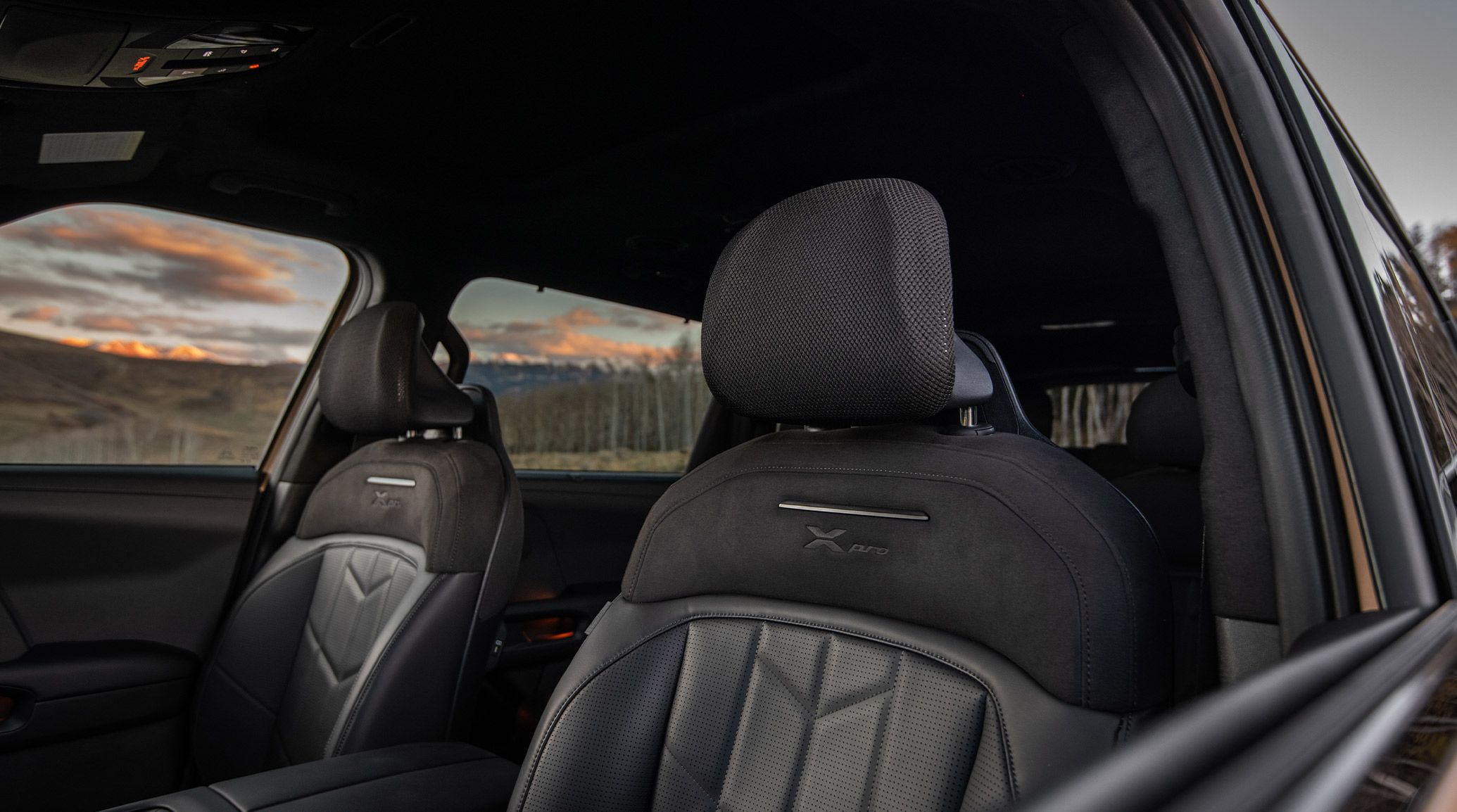 Interior view of the 2027 Kia Telluride X-Pro front seats in black featuring mesh headrests and suede seat trim, with trees and the sunset visible through the windows.