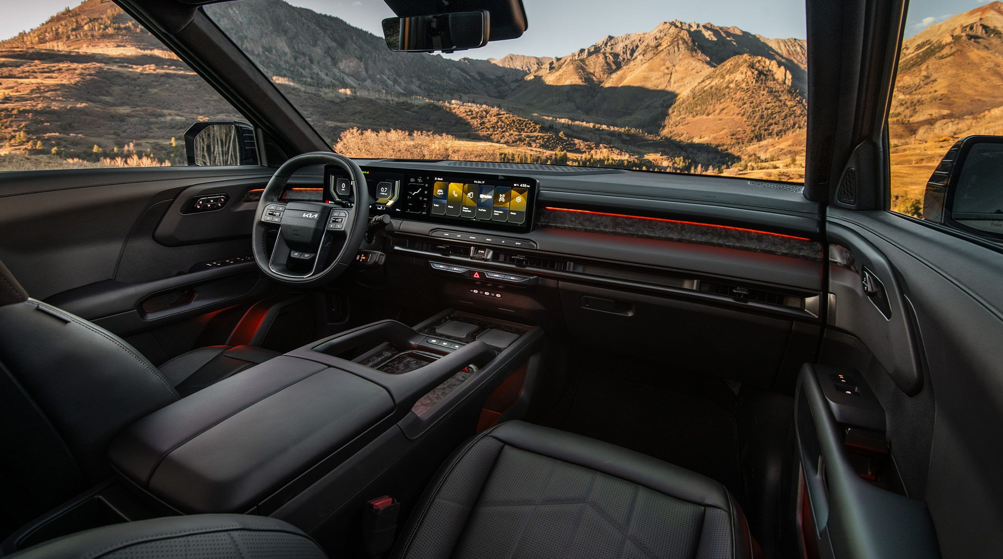 Interior shot of the Kia Telluride showcasing its black suede seats, panoramic digital display, and premium dashboard design with mountain scenery visible through the windows.