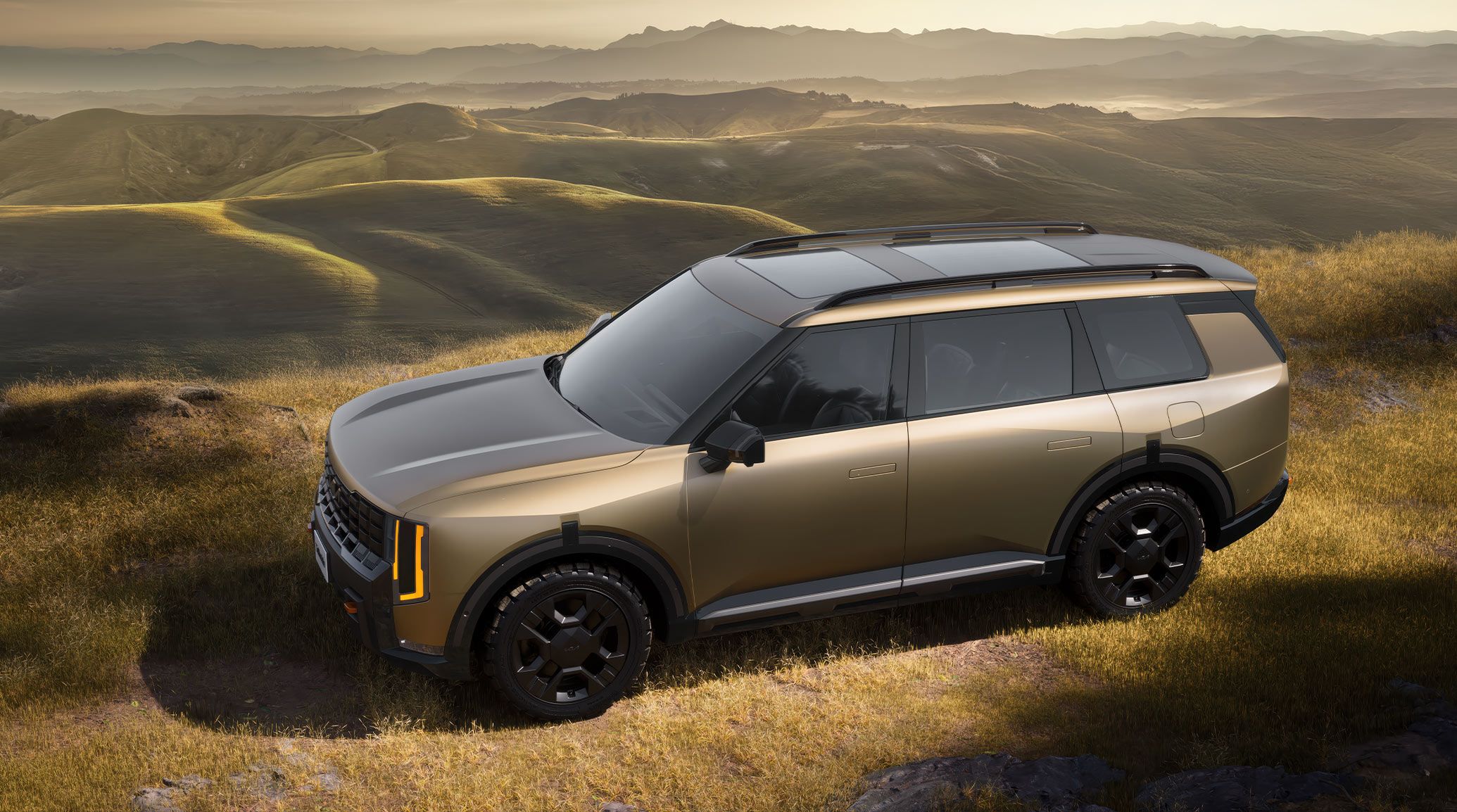 2027 Kia Telluride X-Pro SX Prestige in brown with black accents, featuring bold vertical LED headlights, black alloy wheels, and roof rails, parked on a grassy hilltop with panoramic lush mountain views.