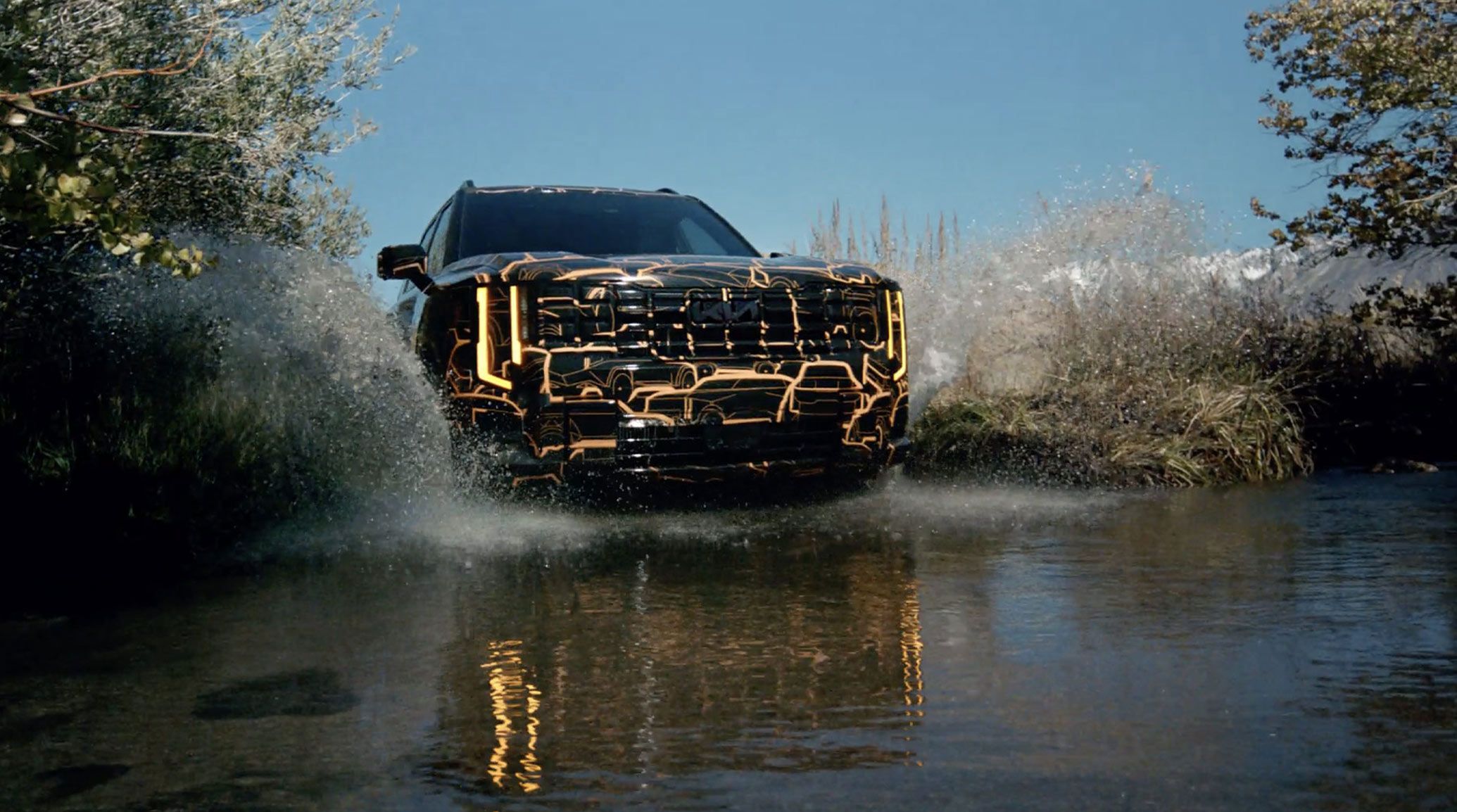 Dynamic shot of the 2027 Kia Telluride in glossy black with orange Telluride graphic accents, driving into a lake and showcasing its bold front design, signature grille, and rugged SUV design.
