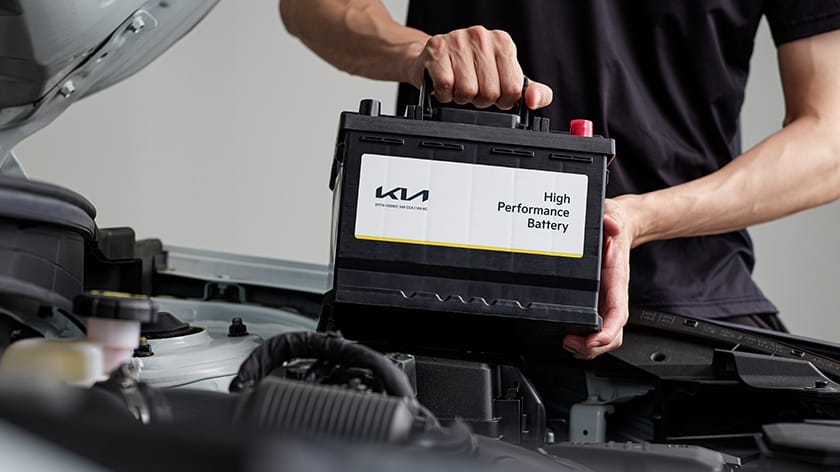 Un técnico sostiene una batería original Kia de 12 V bajo el capó.