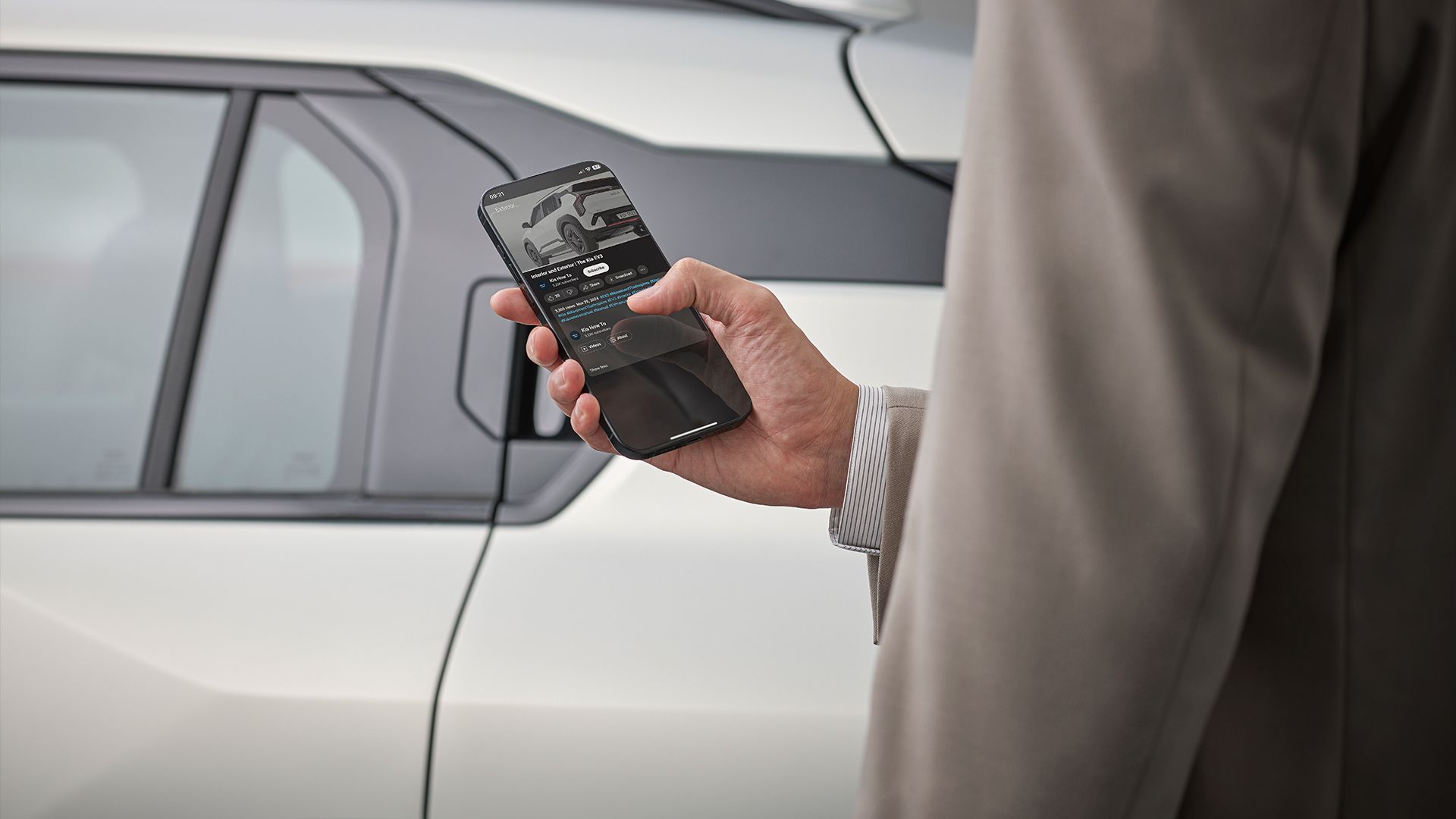 A person watching a Kia EV3 how-to video on a smartphone while standing beside the EV3